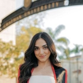 Headshot portrait of Saba Modaressi smiling in a graduation gown under a university arch