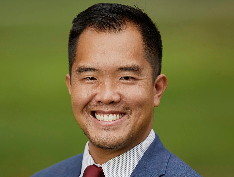 Headshot portrait of a smiling man named Ngo in a blue suit against a green background