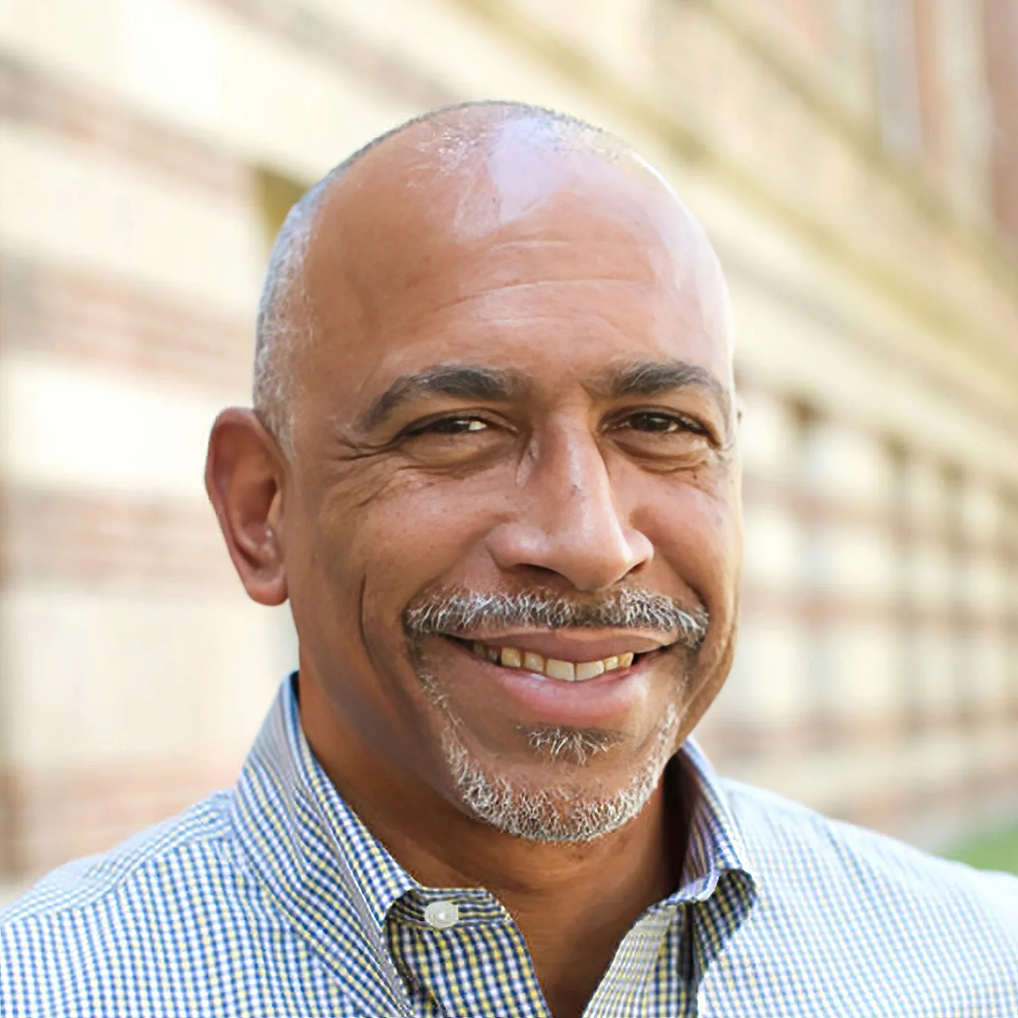 Headshot portrait of Pedro Noguera smiling outdoors near a brick building
