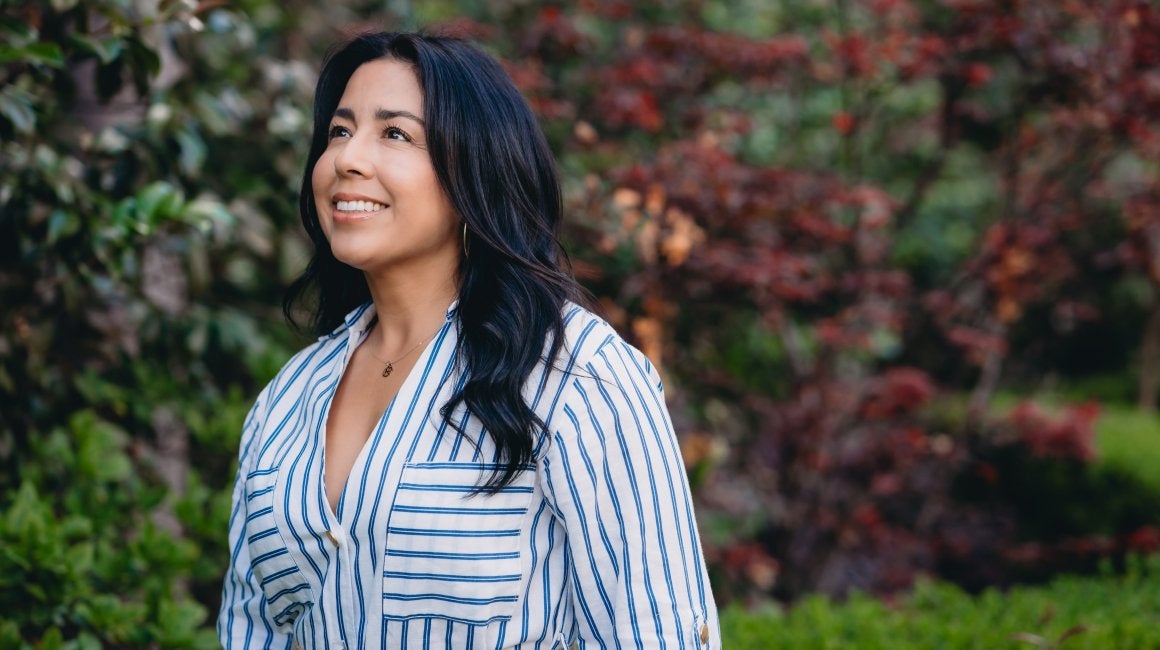 Woman in a striped shirt smiling and looking upward outdoors near red and green foliage
