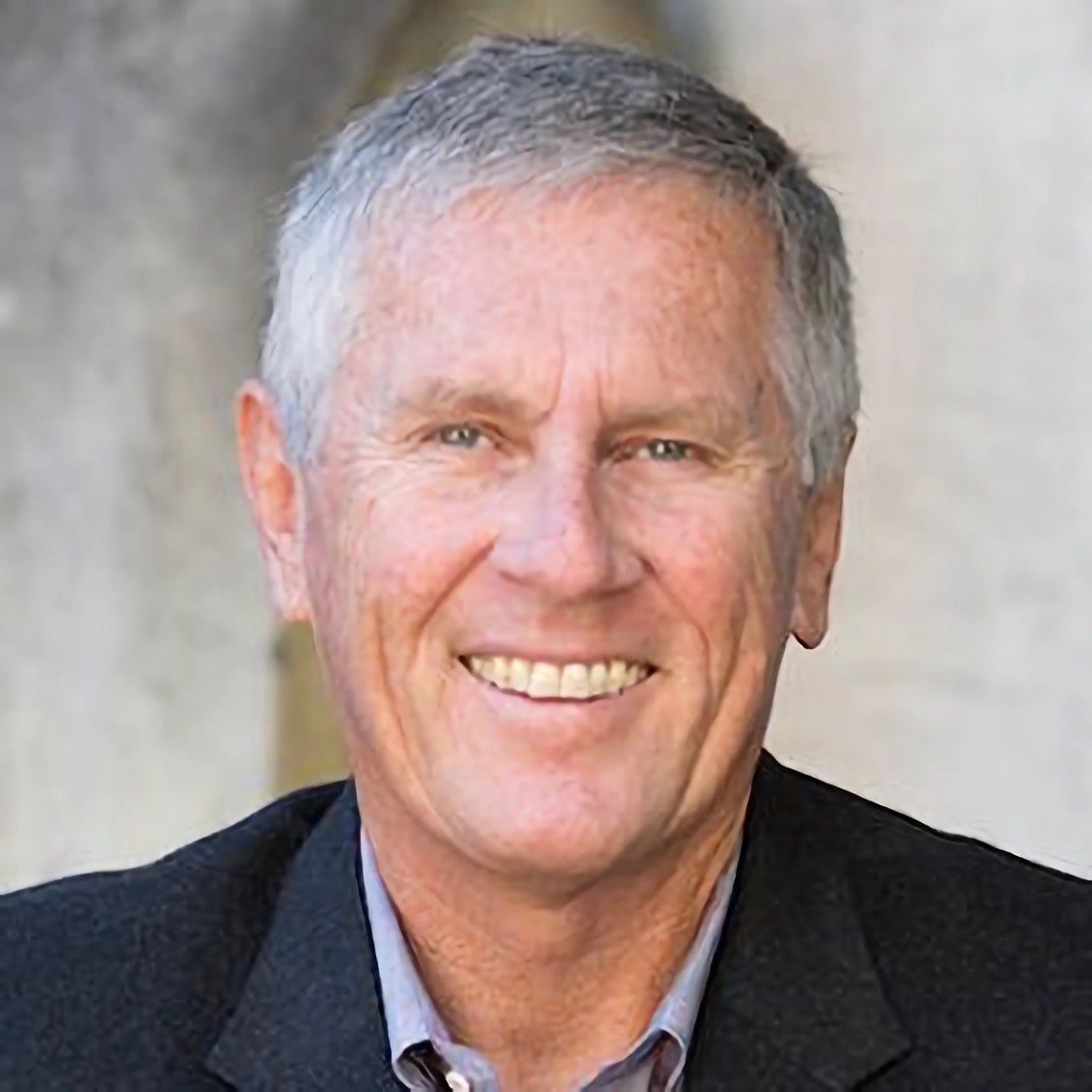 Headshot portrait of David Cash smiling in a dark blazer near a campus archway