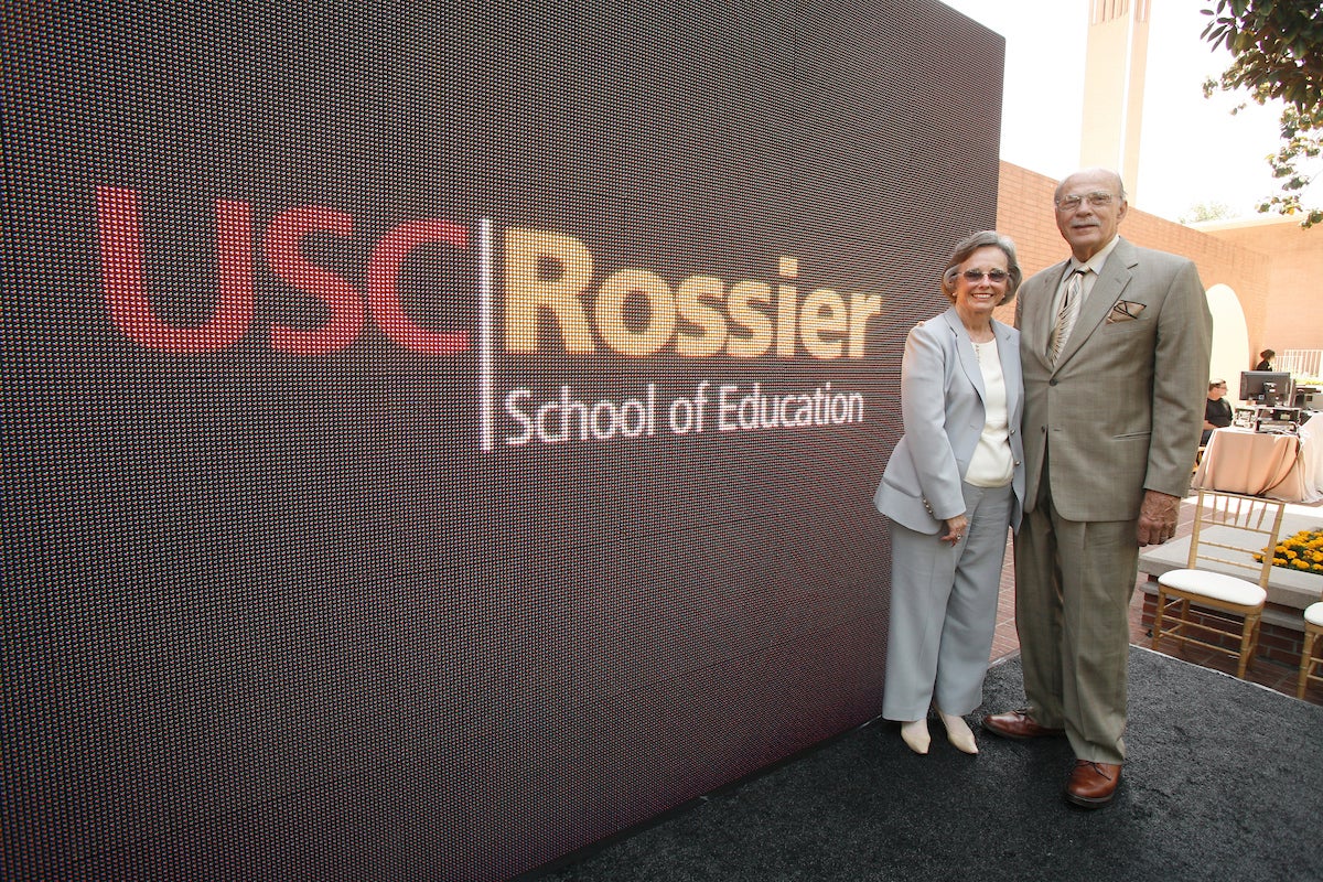 Roger and Barbara Rossier standing near the USC Rossier School of Education sign