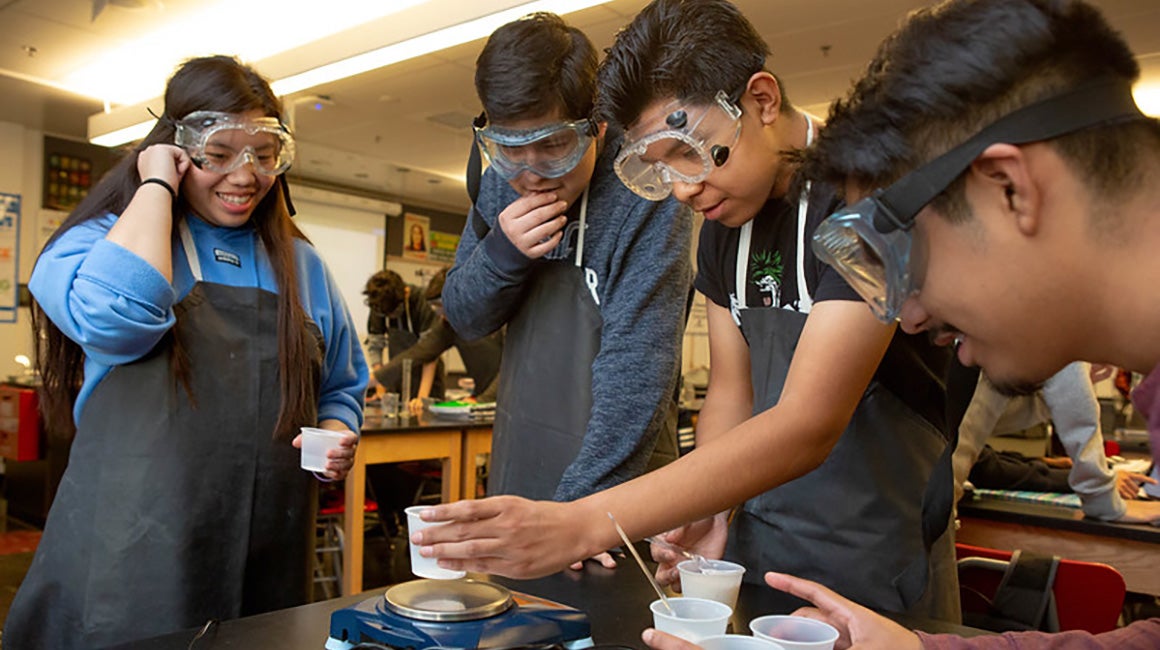 Students wearing aprons conducting a science experiment in class